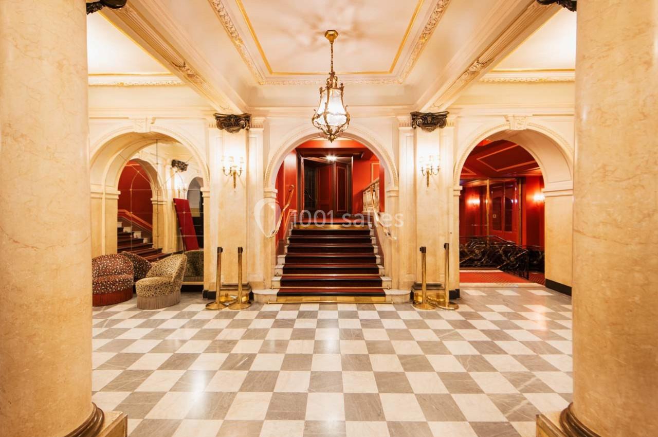 Hall d'entrée élégant avec colonnes en marbre, sol à carreaux, escalier central et éclairage suspendu.