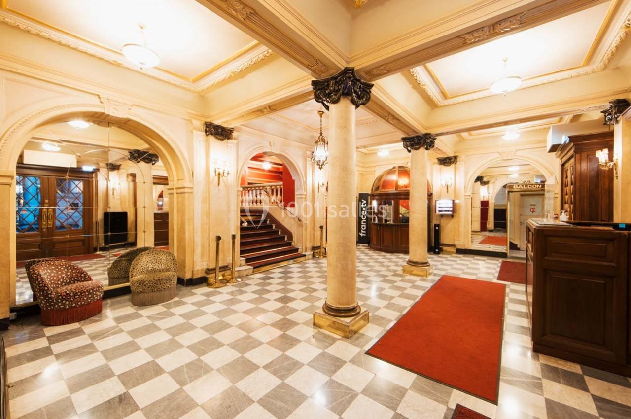 Hall d'entrée spacieux avec colonnes, sol en marbre, tapis rouges, fauteuils et escalier menant à l'étage.