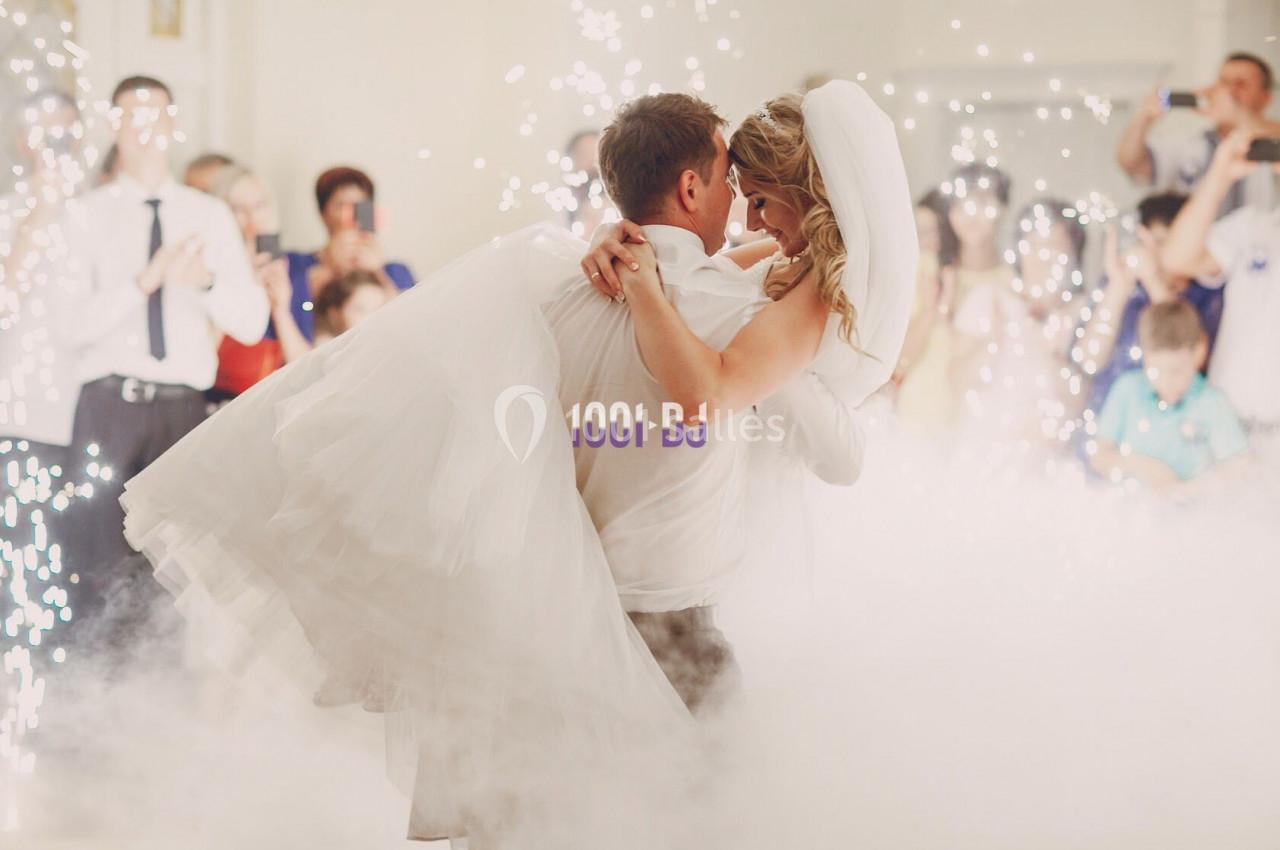 Un couple de mariés danse au milieu de la fumée et des étincelles, entouré d'invités.