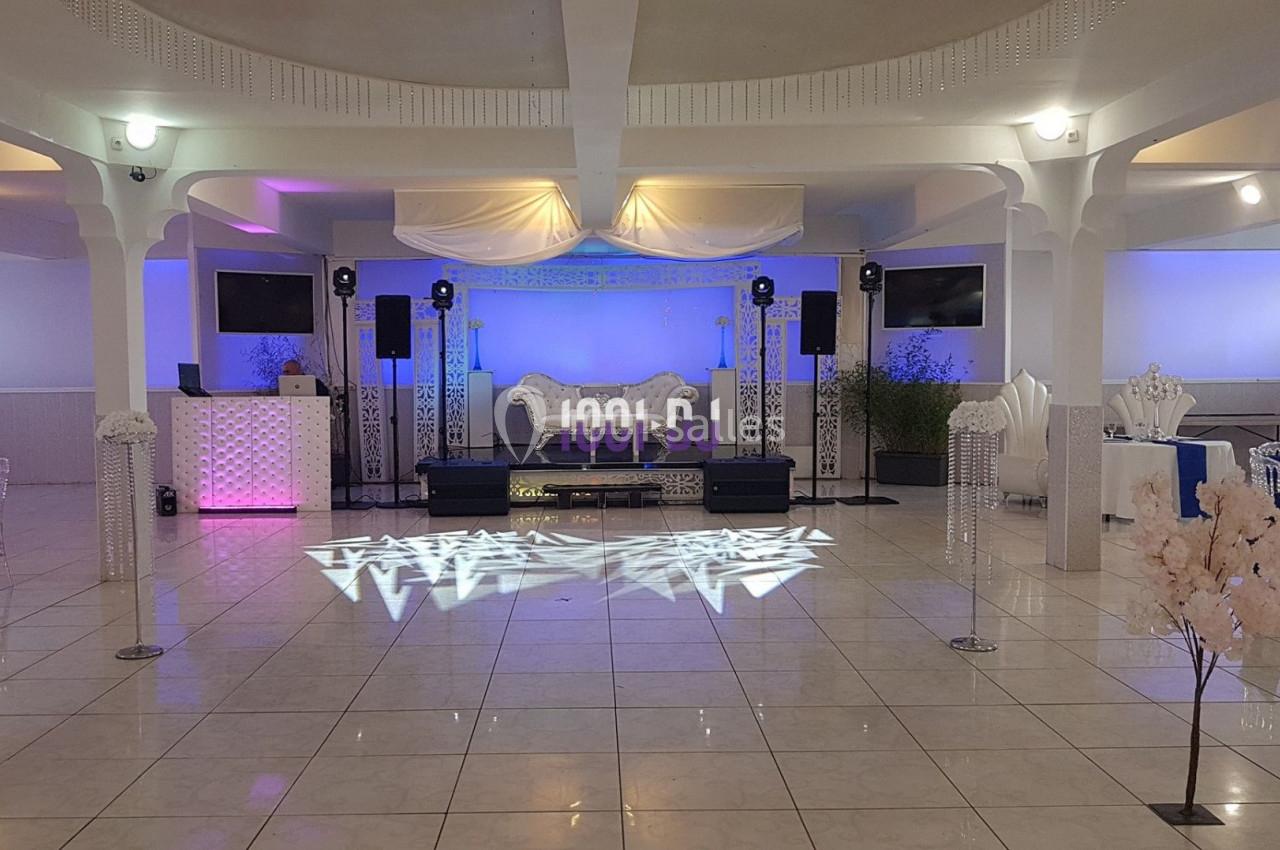 Salle de réception décorée avec des éclairages colorés, une scène équipée de haut-parleurs et un sol carrelé brillant.