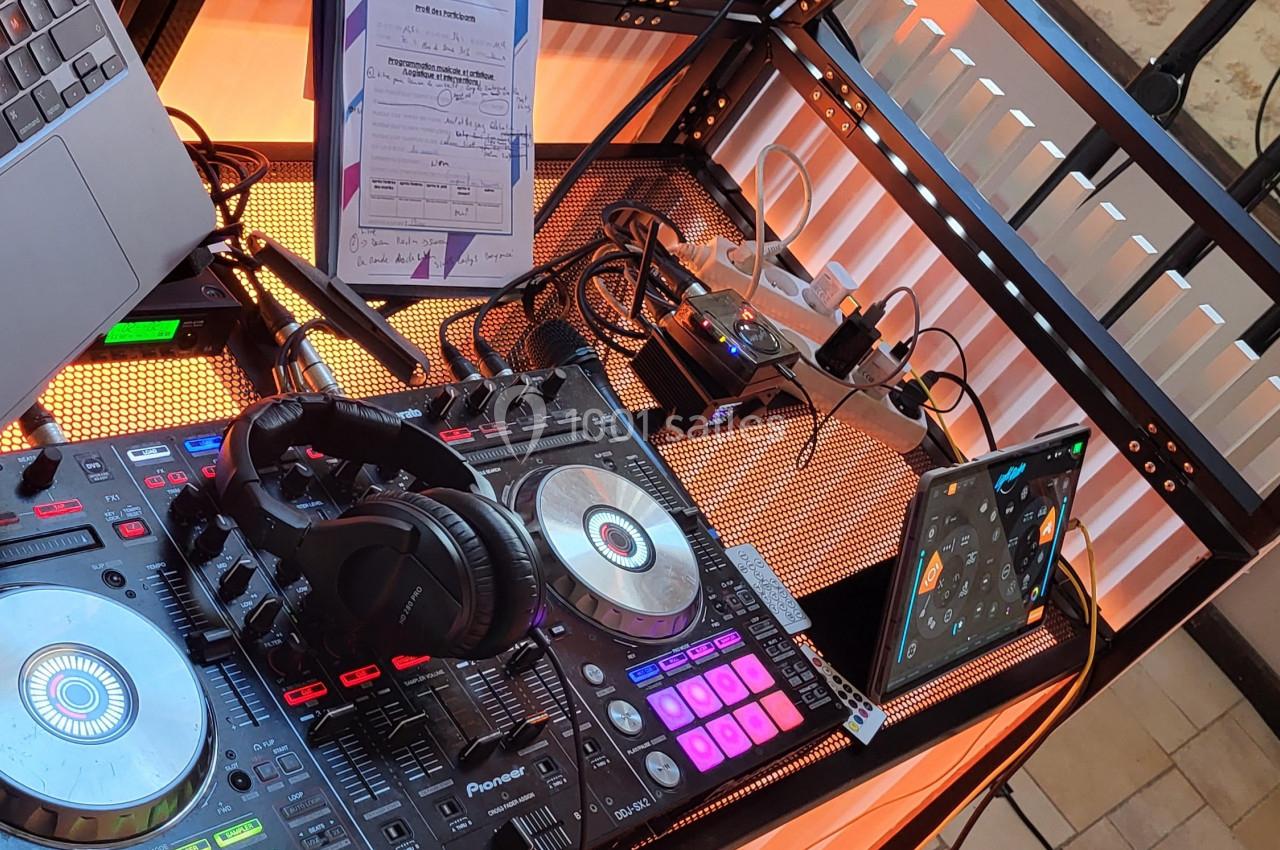Poste de DJ avec platines, casque audio, tablette et câblage, installé sur une table éclairée par des lumières colorées.