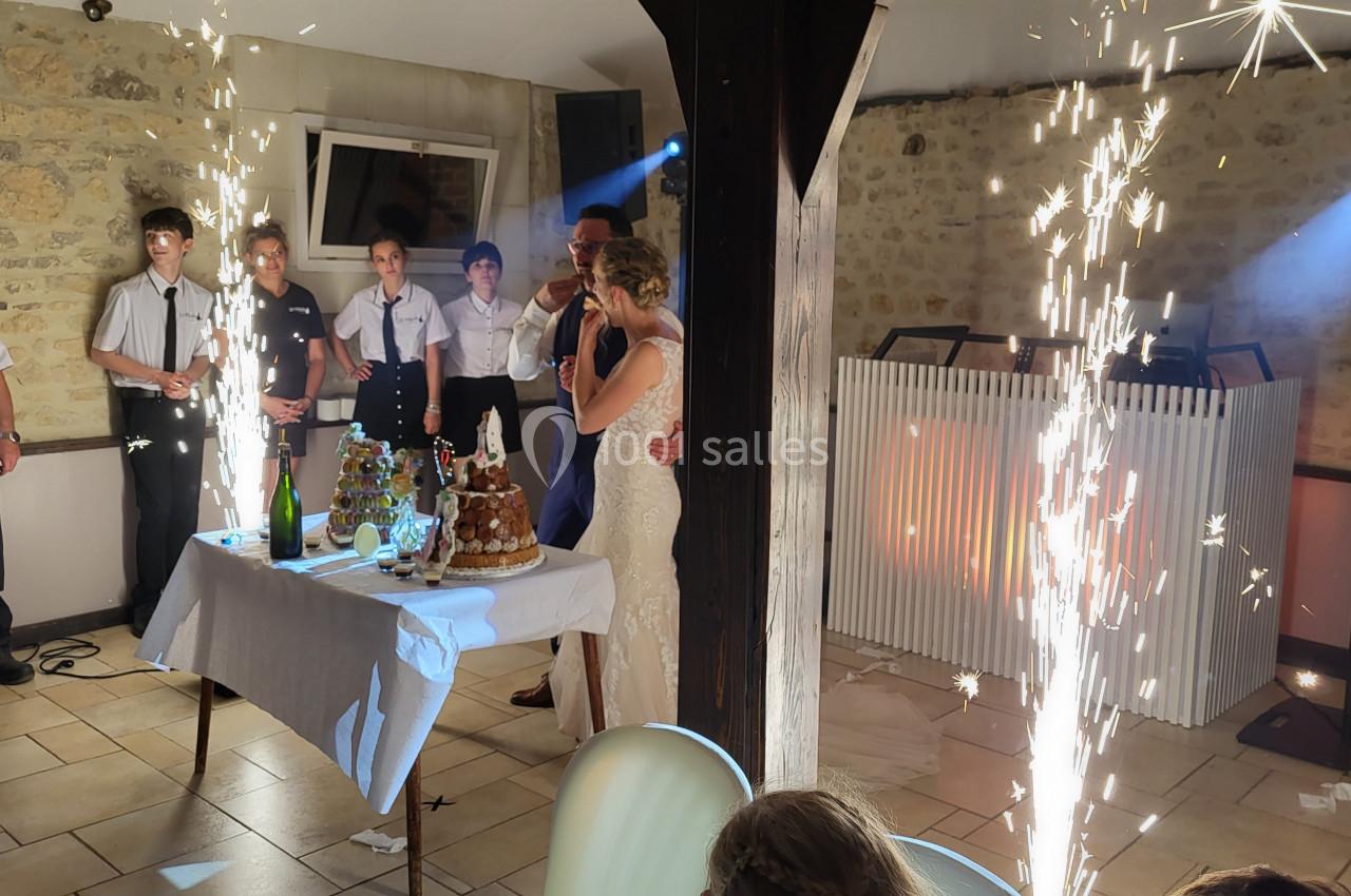 Un couple de mariés se tient près d'une table de desserts avec des fontaines lumineuses, entouré d'invités dans une salle en…