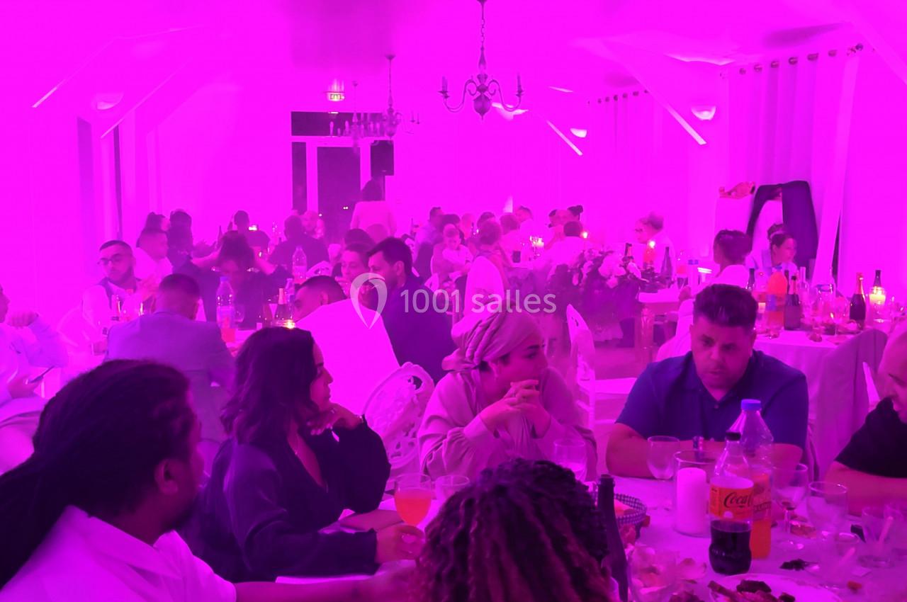 Des convives assis à des tables rondes dans une salle éclairée par une lumière rose, discutant et partageant un repas.