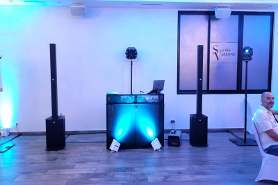 Un homme en chemise blanche et pantalon bleu anime un événement avec un micro dans une salle de réception.