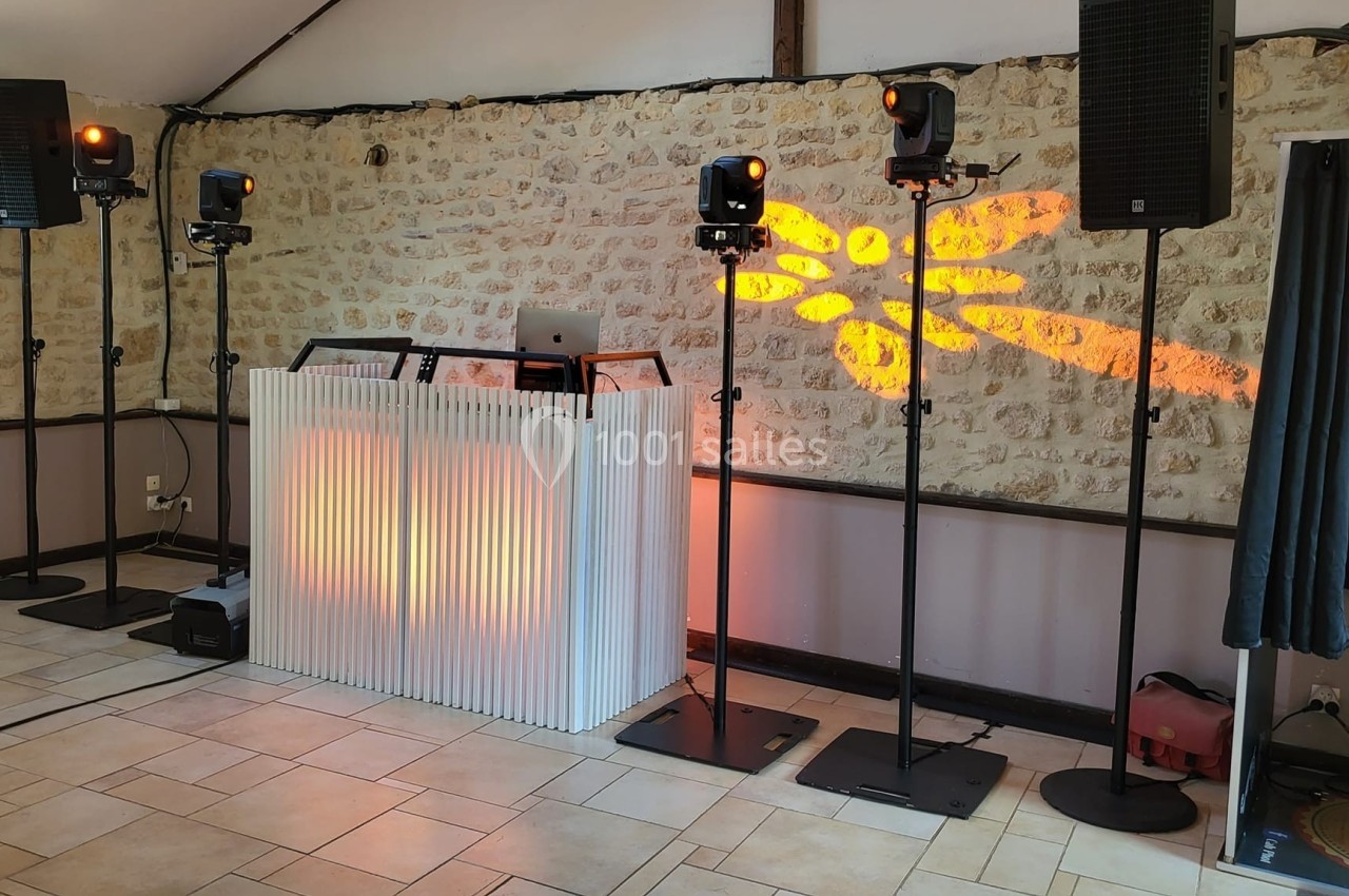 Installation de matériel de sonorisation et éclairage avec une cabine de DJ dans une salle aux murs en pierre.