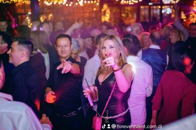 Un homme en chemise blanche et pantalon bleu anime un événement avec un micro dans une salle de réception.