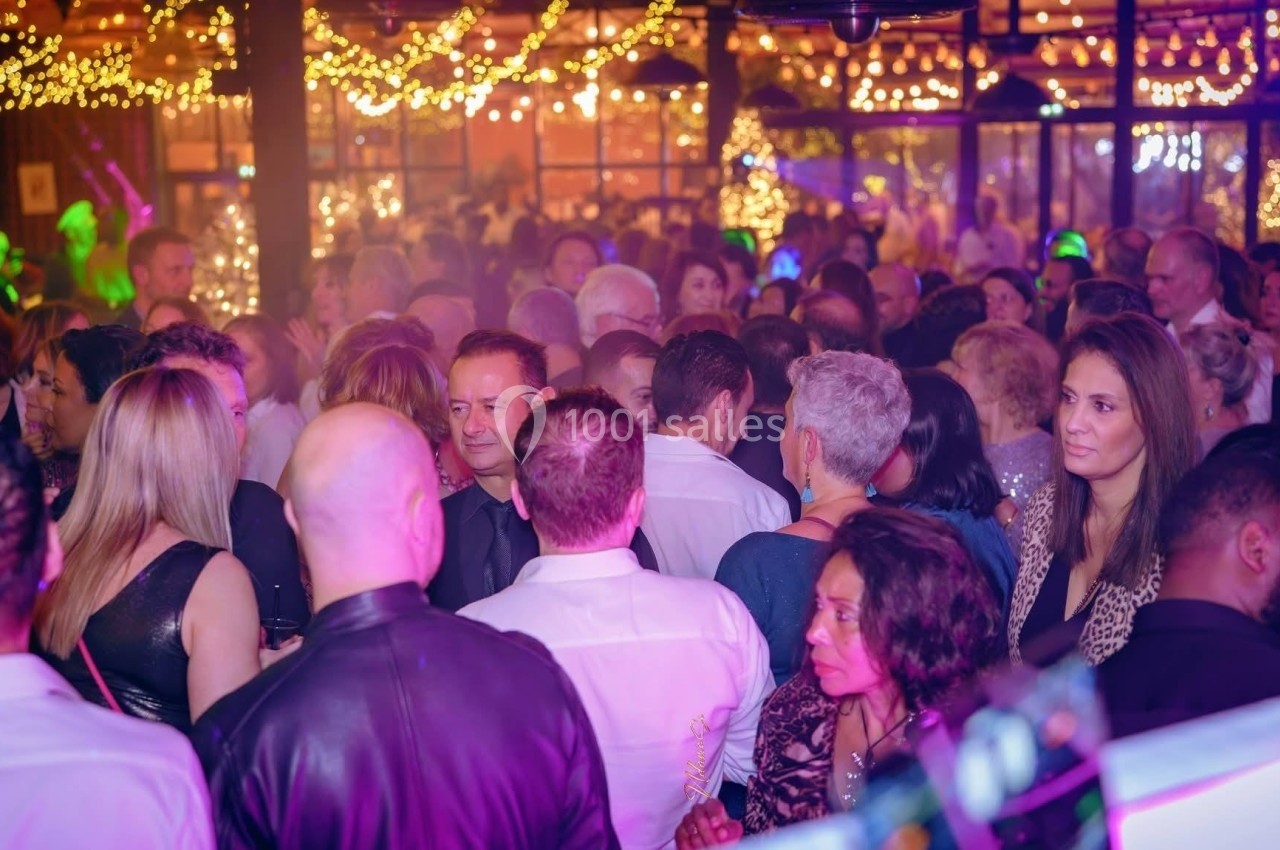 Foule de personnes dans un lieu festif éclairé par des guirlandes lumineuses, ambiance animée et conviviale.