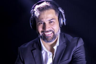 Miniature DJ Garwell Homme souriant portant un casque audio et un costume sombre, éclairé par une lumière douce sur fond noir.