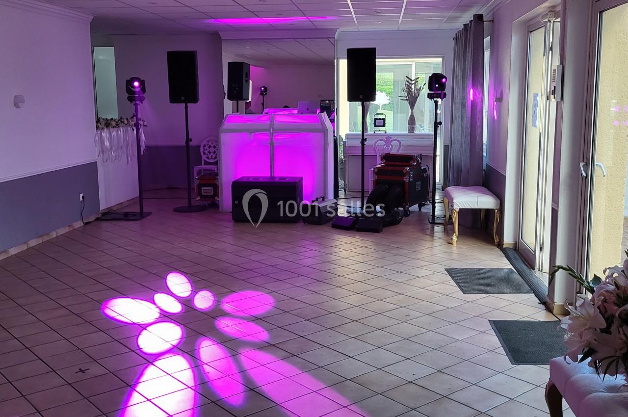 Salle de réception avec piste de danse, éclairage violet, équipement audio et décoration florale.