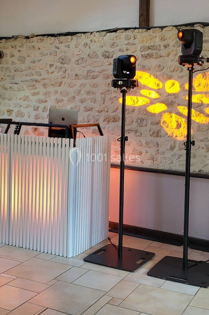 Pupitre de DJ blanc avec deux projecteurs lumineux diffusant des motifs orange sur un mur en pierre.