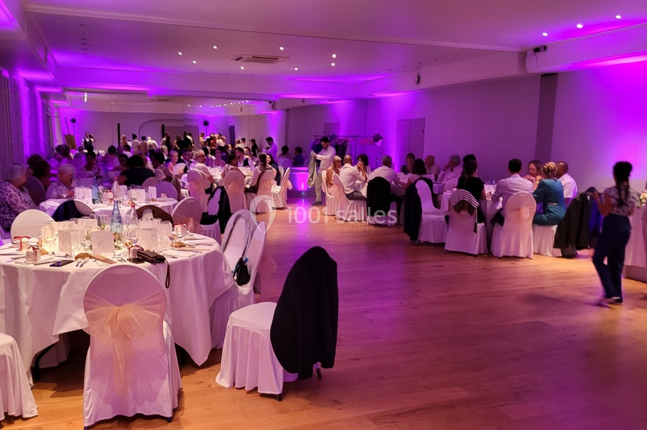 Salle de réception avec des tables dressées et des convives assis, éclairée par une lumière violette.