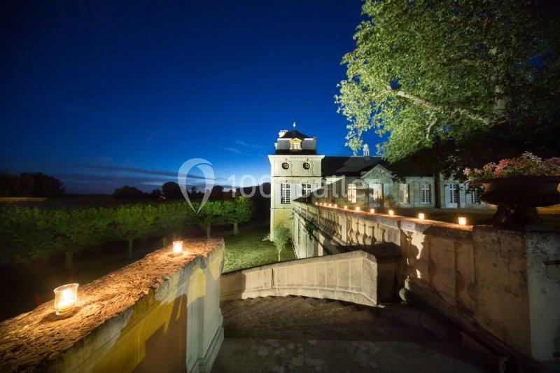 Manoir éclairé la nuit, entouré d'arbres, avec des bougies allumées le long d'un escalier en pierre.