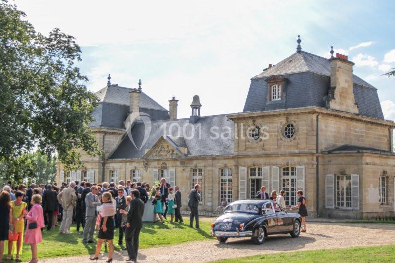 Groupe de personnes rassemblées devant un bâtiment historique en pierre, avec une voiture ancienne garée au premier plan.