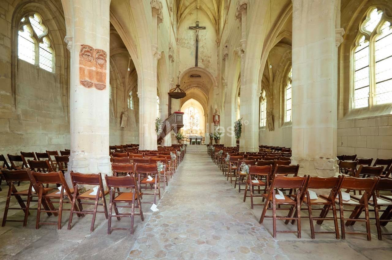 Intérieur d'une église avec des rangées de chaises en bois, un autel décoré et des vitraux laissant entrer la lumière.