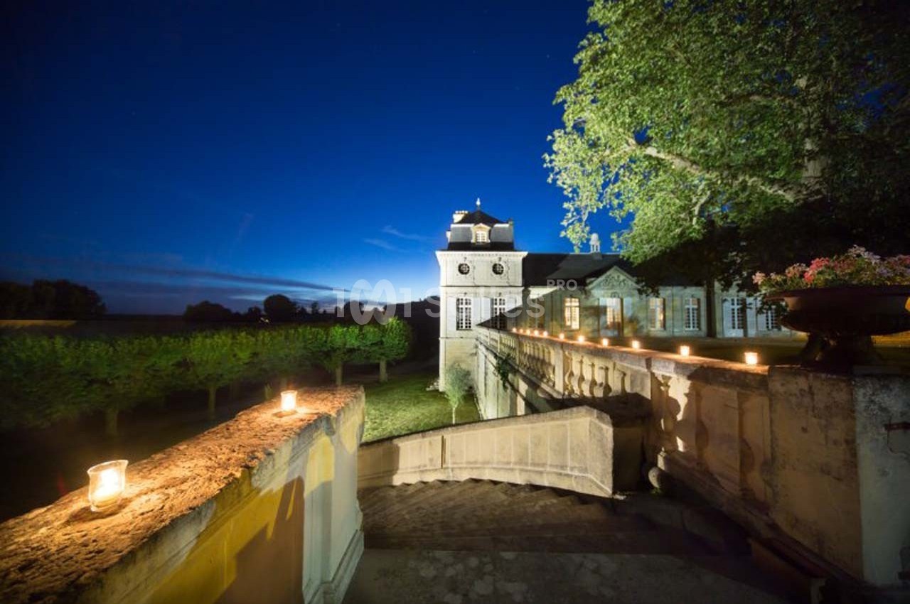 Château éclairé la nuit, entouré de vignes, avec des bougies disposées sur un muret en pierre.