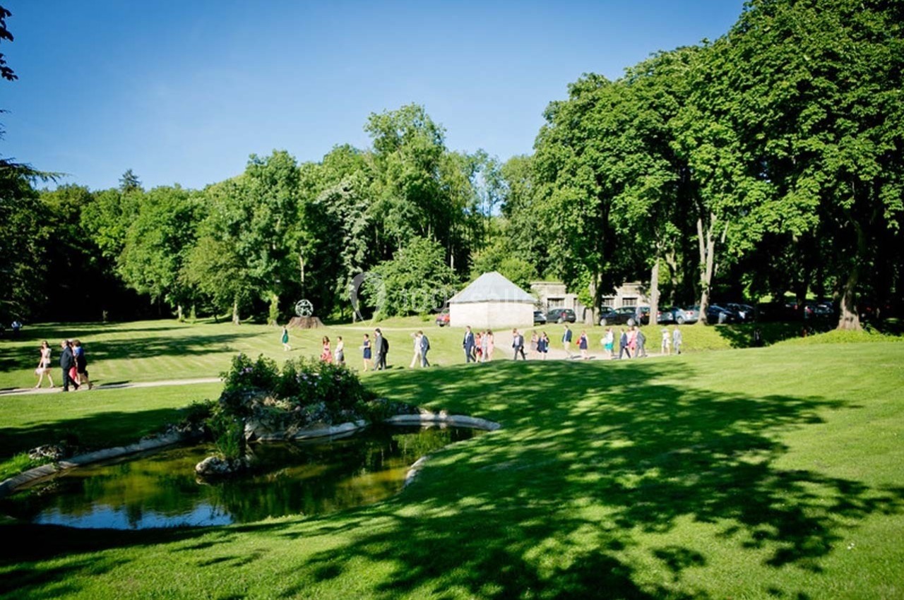 Un groupe de personnes marche dans un parc verdoyant avec une petite mare au premier plan et des arbres en arrière-plan.