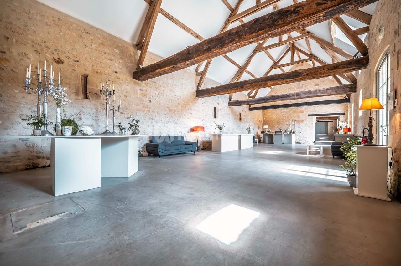 Salle spacieuse avec murs en pierre, poutres apparentes, mobilier moderne et lumière naturelle abondante.