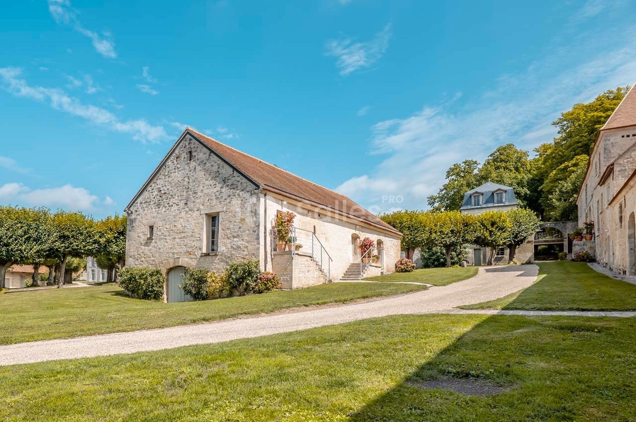 Bâtiment en pierre avec toit en tuiles, entouré de pelouse et d'arbres sous un ciel bleu dégagé.
