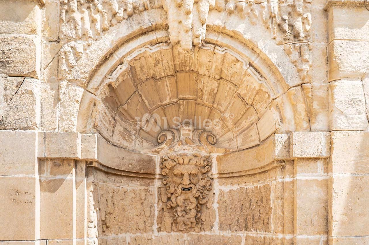 Sculpture en pierre représentant un visage entouré d'ornements sous une arche voûtée d'un bâtiment ancien.