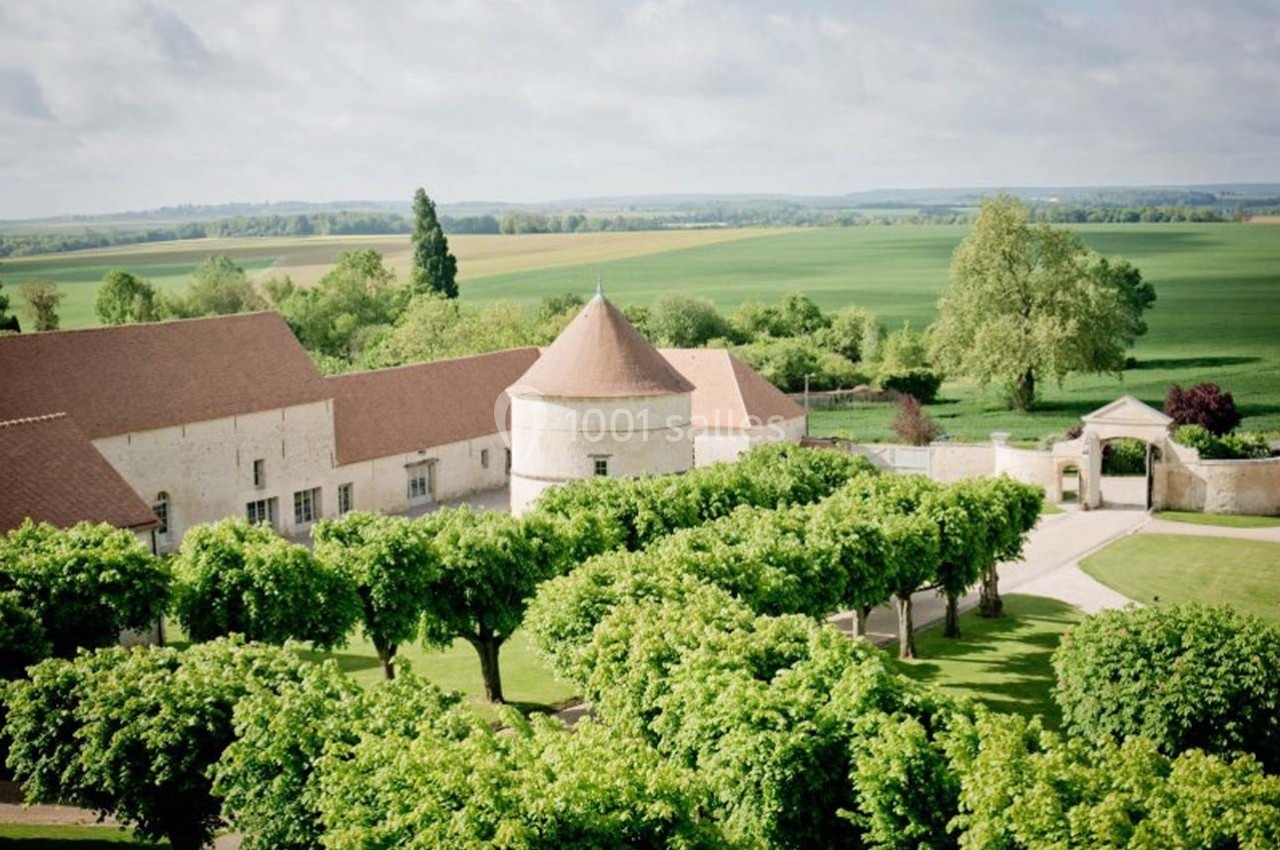 Vue aérienne d'un domaine rural avec bâtiments en pierre, toits en tuiles rouges, allée bordée d'arbres et champs verdoyants.