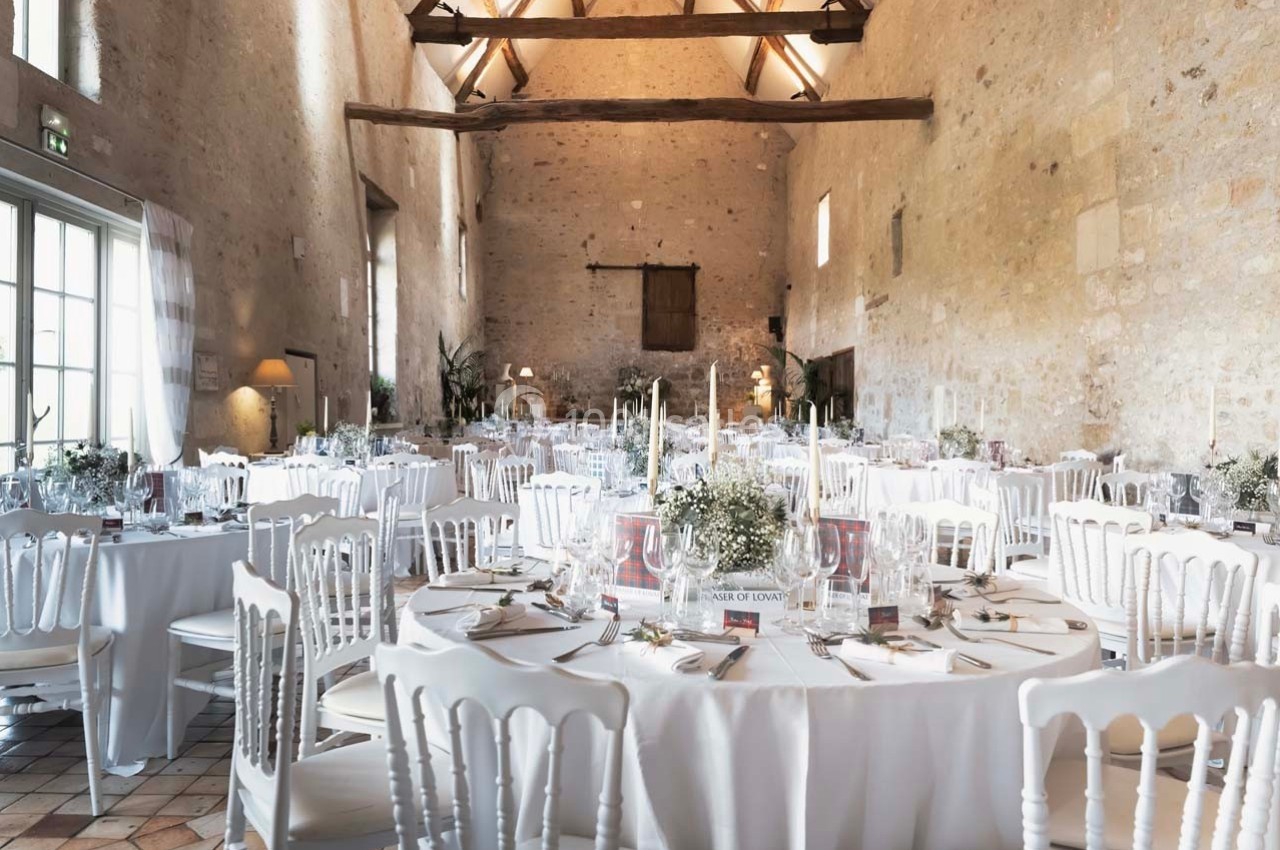 Salle de réception lumineuse avec tables rondes décorées de nappes blanches, bougies et compositions florales.