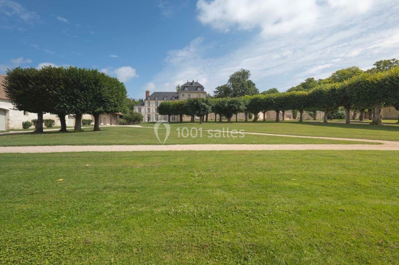 Pelouse bien entretenue avec allées gravillonnées, bordée d'arbres taillés, menant à un bâtiment historique sous un ciel…