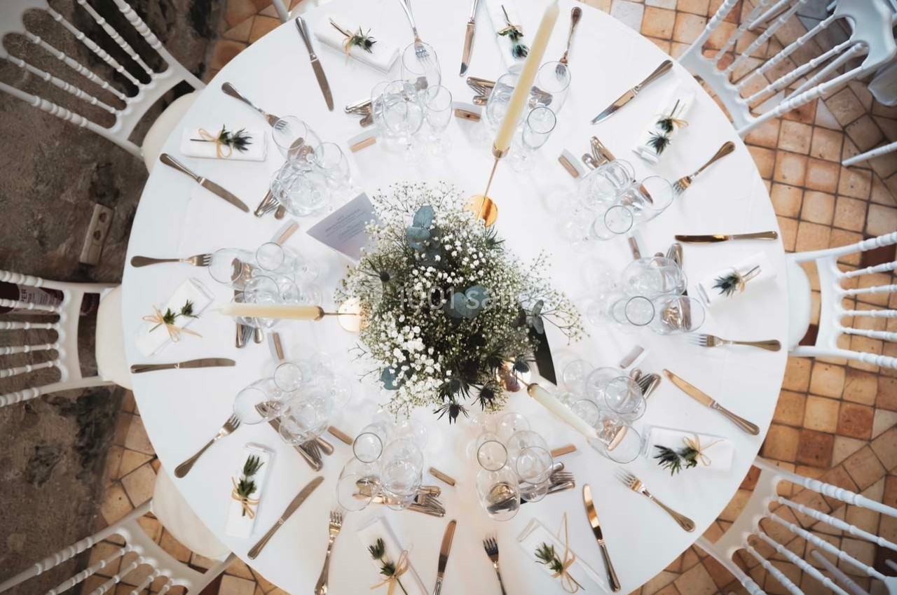 Table ronde décorée pour un événement, avec vaisselle, couverts, bougies et centre de table floral.