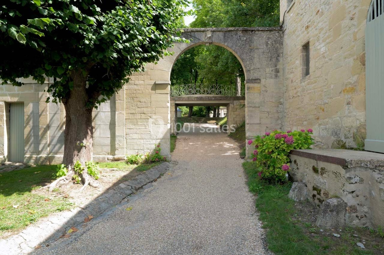 Chemin gravillonné bordé de verdure et de fleurs, passant sous une arche en pierre dans un cadre paisible.