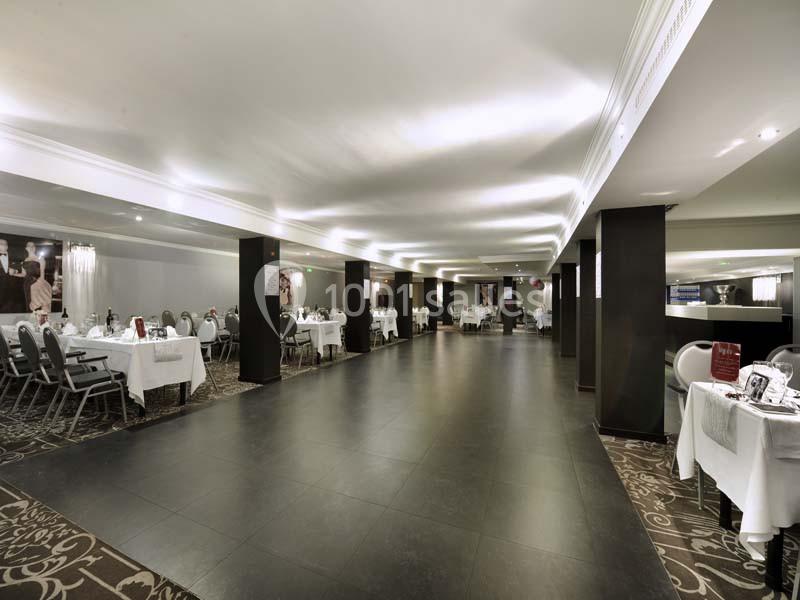Salle de réception spacieuse avec tables dressées, chaises grises et éclairage moderne.