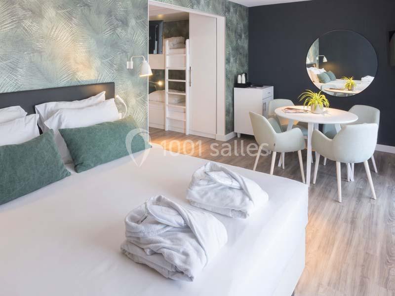 Chambre d'hôtel moderne avec lit double, lits superposés, table ronde, chaises et décoration aux tons verts.