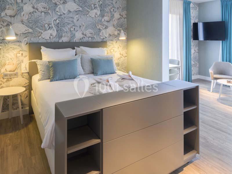 Chambre lumineuse avec lit double, papier peint à motifs de flamants roses, mobilier moderne et télévision murale.
