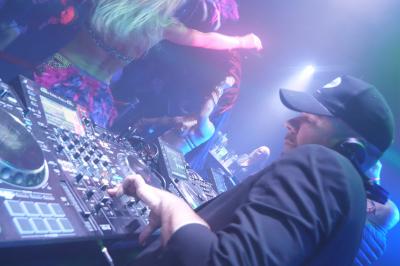 Un DJ mixe sur scène dans une ambiance sombre et lumineuse, décorée avec des éléments d'Halloween.