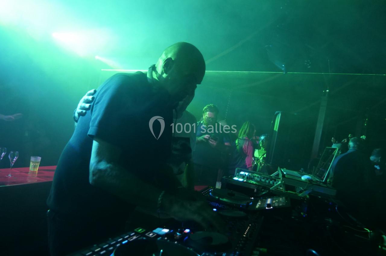 Un DJ mixe sur une table de mixage dans une ambiance lumineuse verte, entouré de personnes en arrière-plan.