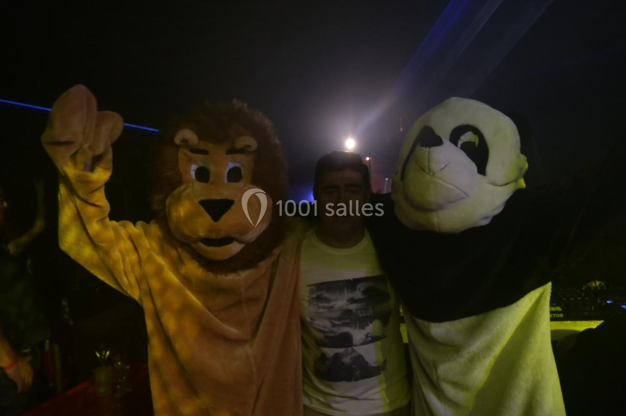 Un homme pose entre deux personnes déguisées en lion et en panda dans un environnement sombre avec des lumières.