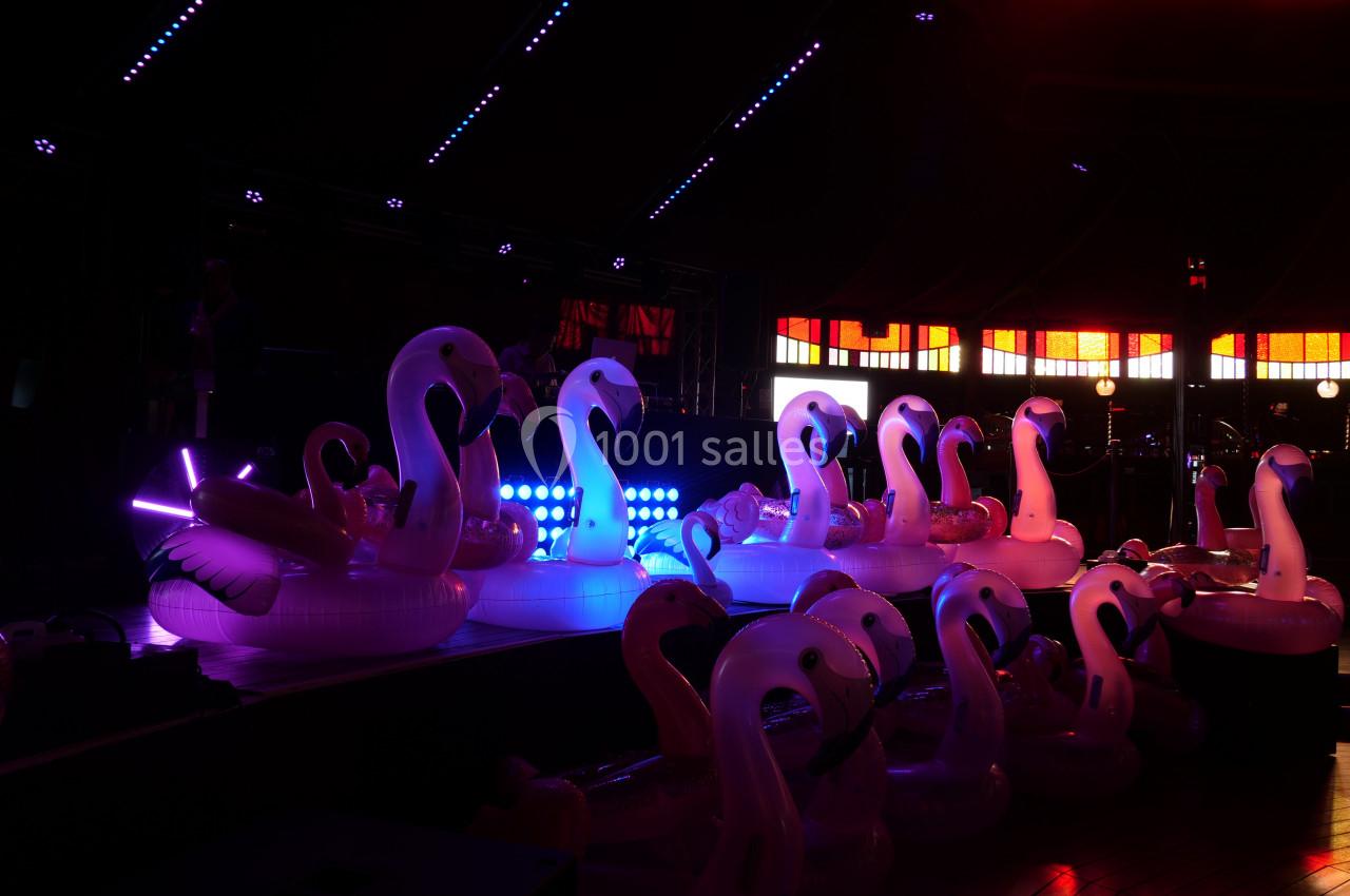 Des bouées flamants roses éclairées par des lumières colorées dans un espace sombre avec des vitraux en arrière-plan.