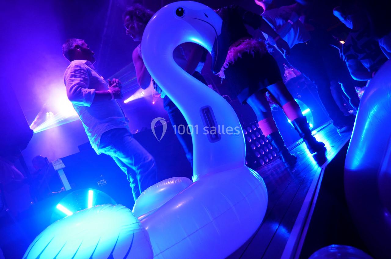 Personnes dansant dans une ambiance lumineuse bleutée avec une bouée en forme de cygne au premier plan.