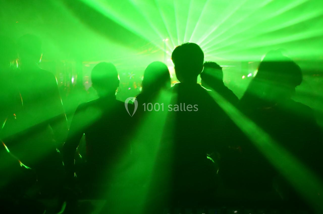 Silhouettes de personnes dans une ambiance festive avec des faisceaux lumineux verts.