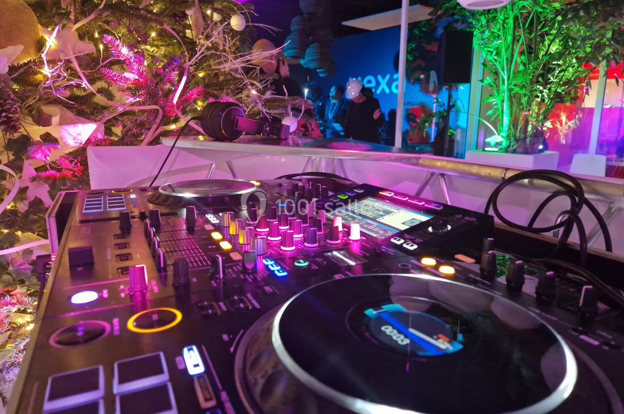 Table de mixage éclairée avec des lumières colorées, entourée de décorations végétales et d'une ambiance festive.