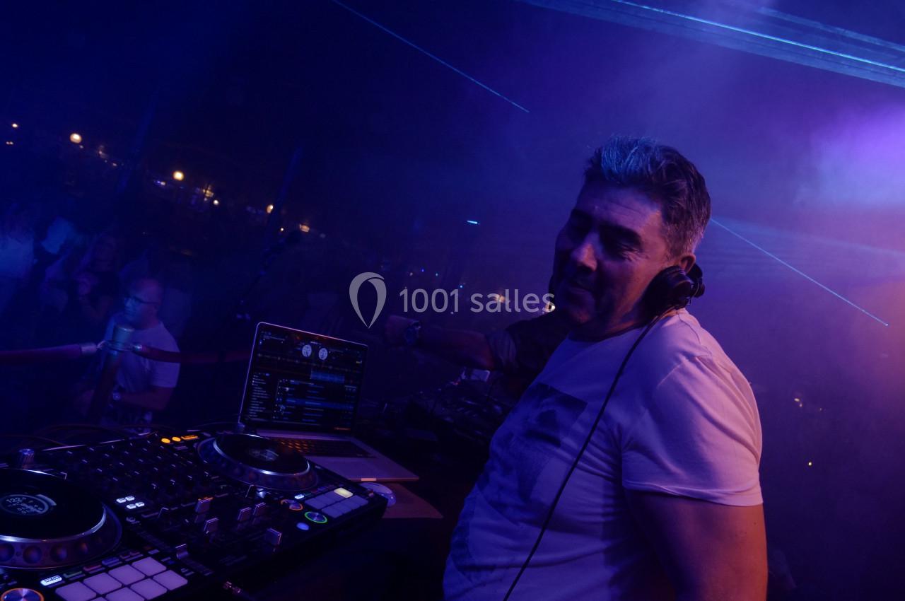 Un DJ mixe sur une scène sombre, entouré d'équipements audio et d'effets lumineux.