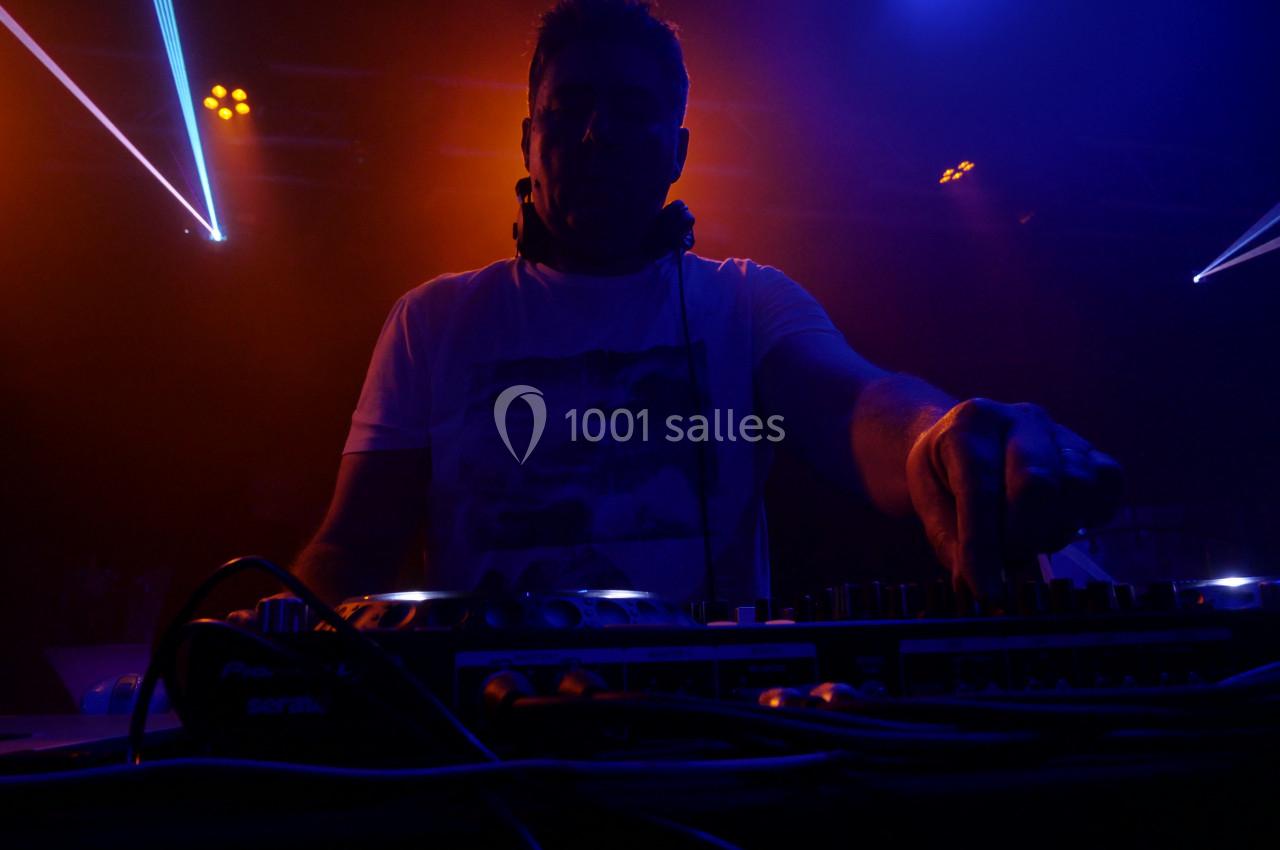 Un DJ mixant sur une console dans une ambiance lumineuse rouge et bleue lors d'une performance en soirée.