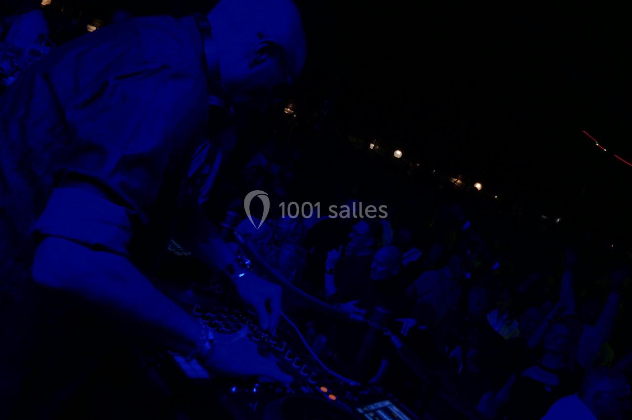 Un DJ mixant sur une table de mixage dans une ambiance sombre, entouré d'un public en arrière-plan.