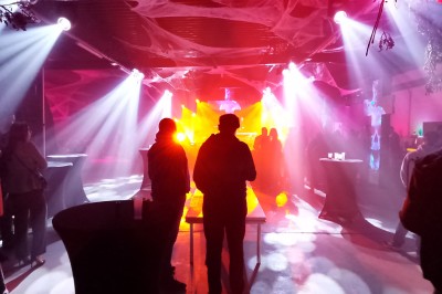 Un DJ mixe sur scène dans une ambiance sombre et lumineuse, décorée avec des éléments d'Halloween.