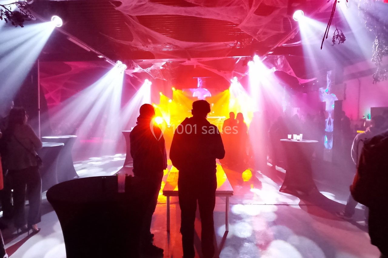 Salle sombre décorée pour une fête, éclairée par des lumières colorées avec des silhouettes de personnes debout.