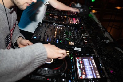 Miniature Equinoxe #33 Un DJ mixe sur une scène éclairée, avec un écran lumineux affichant des motifs rouges en arrière-plan.