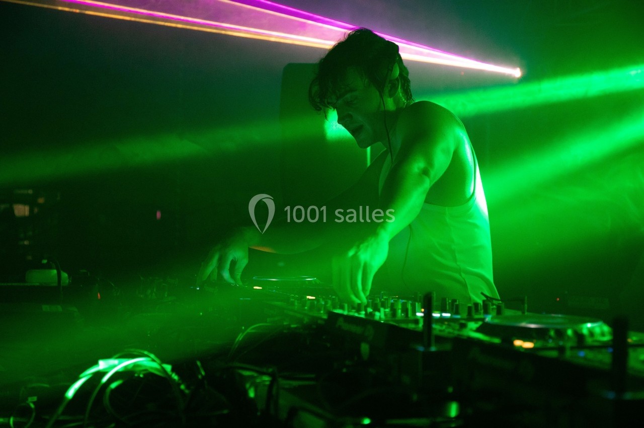 Un DJ mixe de la musique sur une table de mixage dans une ambiance lumineuse verte avec des faisceaux laser.