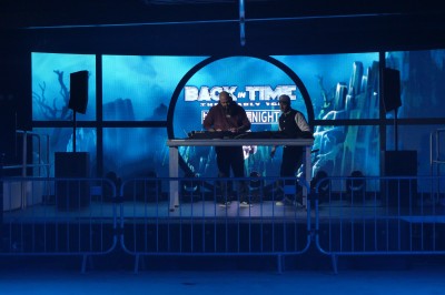 Miniature Equinoxe #36 Un DJ mixe sur une scène éclairée, avec un écran lumineux affichant des motifs rouges en arrière-plan.