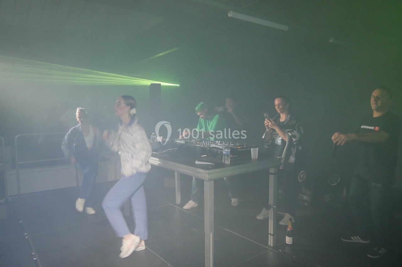 Des personnes dansent et prennent des photos près d'une table de mixage sous des lumières tamisées dans une ambiance festive.