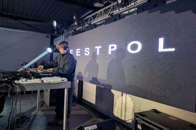 Un DJ mixe sur scène avec des jeux de lumière jaunes et un écran affichant une image de crâne en arrière-plan.