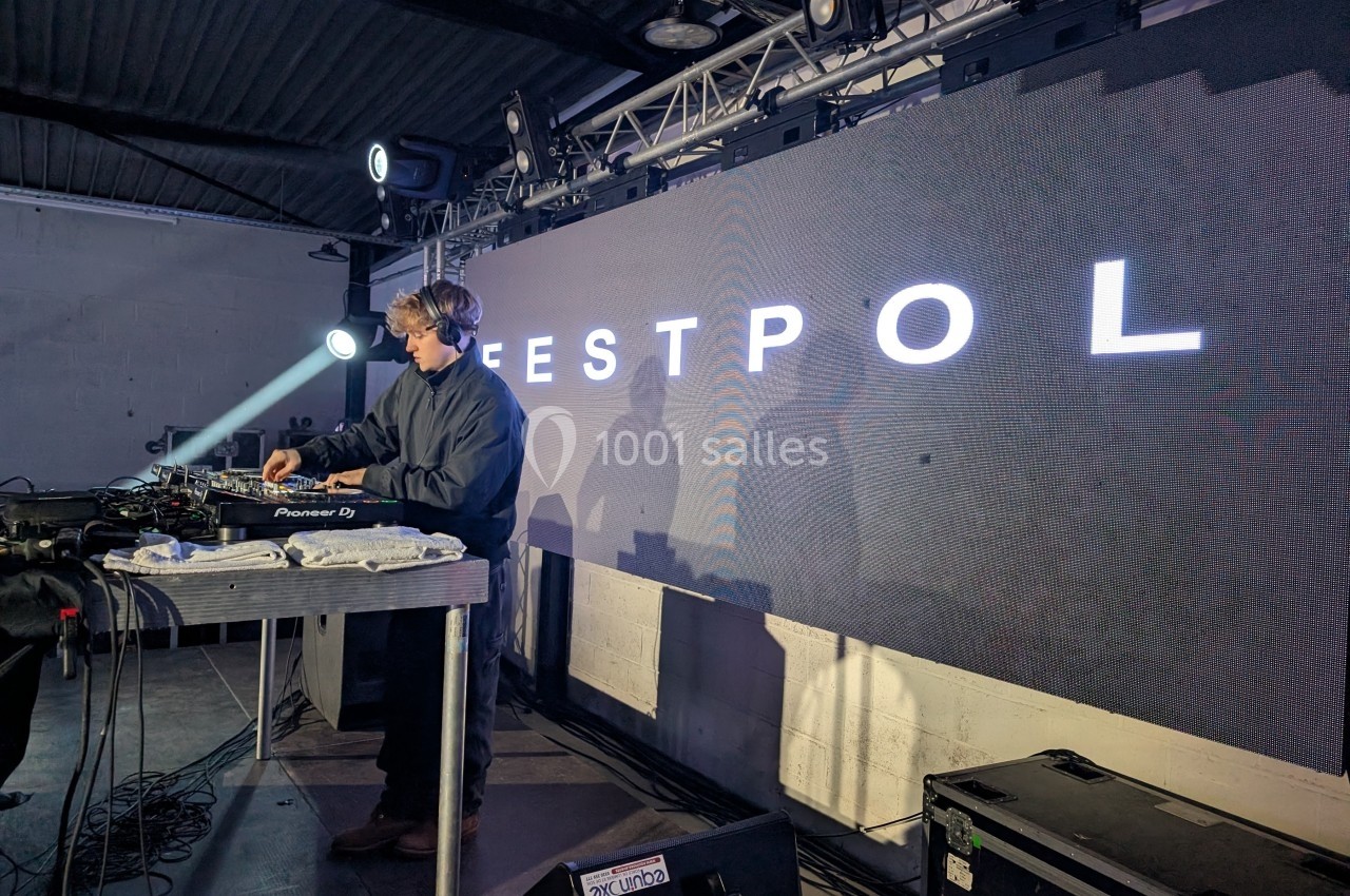 Un DJ mixe sur une scène éclairée devant un écran affichant le mot ’ESTPOL’.