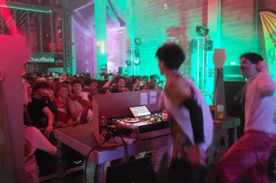 Un DJ mixe sur scène avec des jeux de lumière jaunes et un écran affichant une image de crâne en arrière-plan.